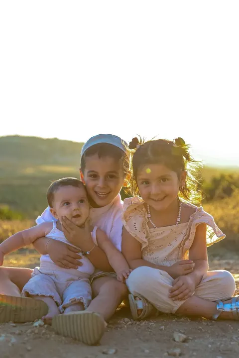 שלושה ילדים יושבים על גבעה באור שקיעה